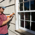 Man caulking window outside of home.