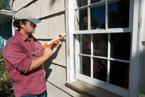 Man caulking window outside of home.